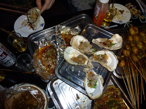 Chengdu barbecue feast: pig's brains (in the tinfoil), oysters, and a variety of things on sticks.